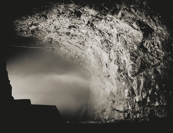Searchlights probing the entrance of a hidden cave at night, with police tape surrounding the area.